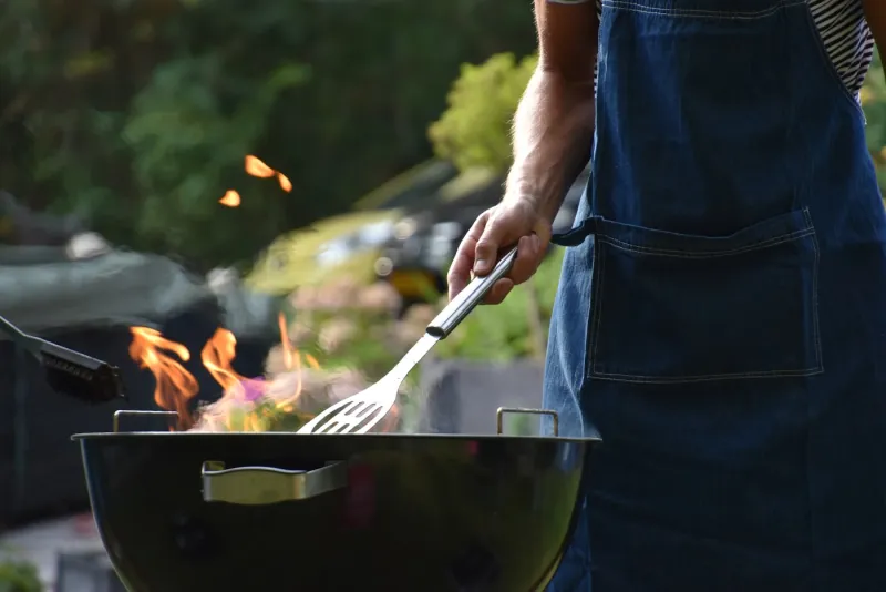 Muž v zástěře griluje na zahradním grilu s plameny