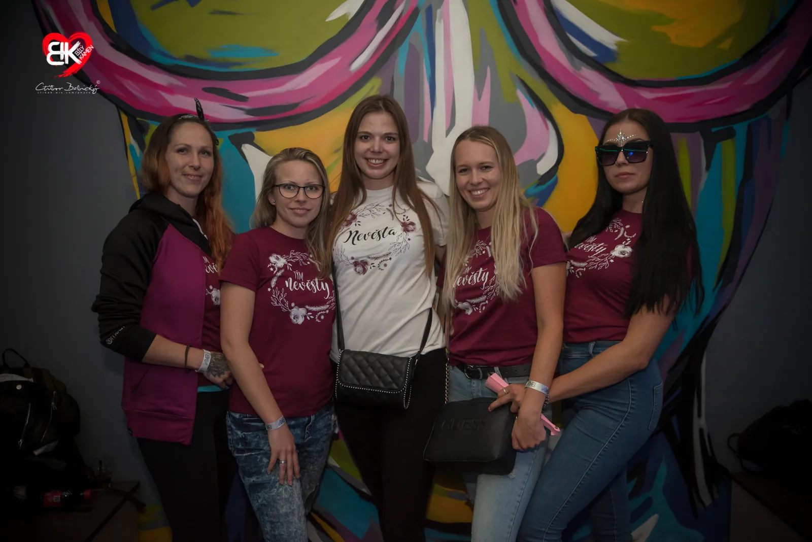 Tým nevěsty ve vínových tričkách před graffiti stěnou klubu